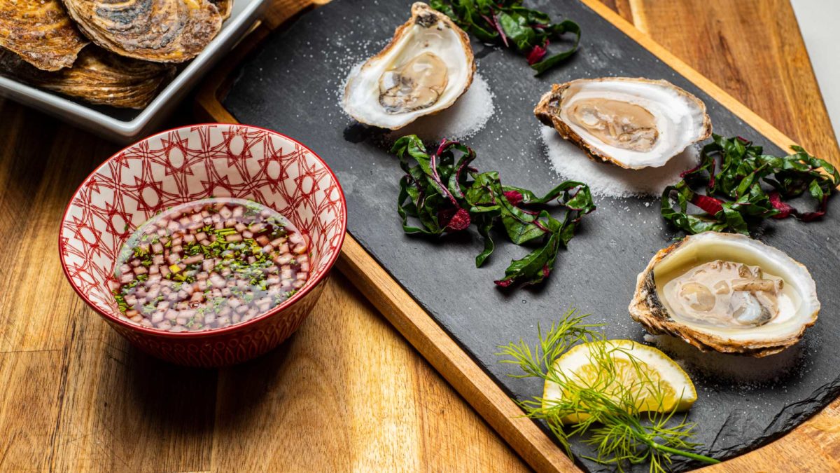 raw halfshell oysters sit on a slate next to prepared Pear and Red Wine Mignonette