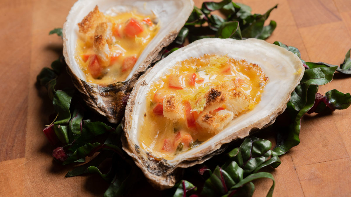 Two half shell baked oysters with red pepper cream sit atop a bed of kale