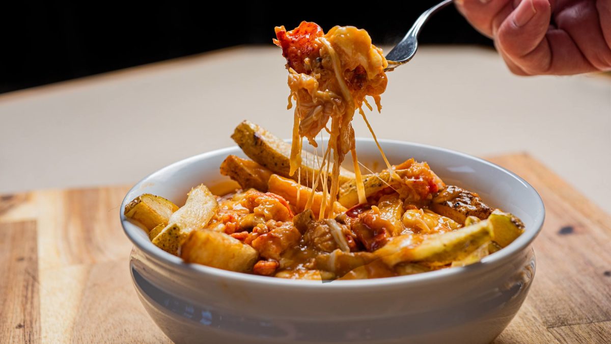 lobster poutine in a bowl. A person pulls some cheese and lobster from it with a fork