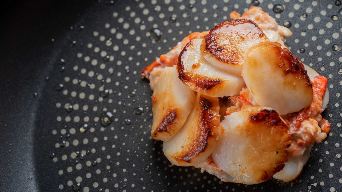 Lobster stuffed scallops sit in a frying pan