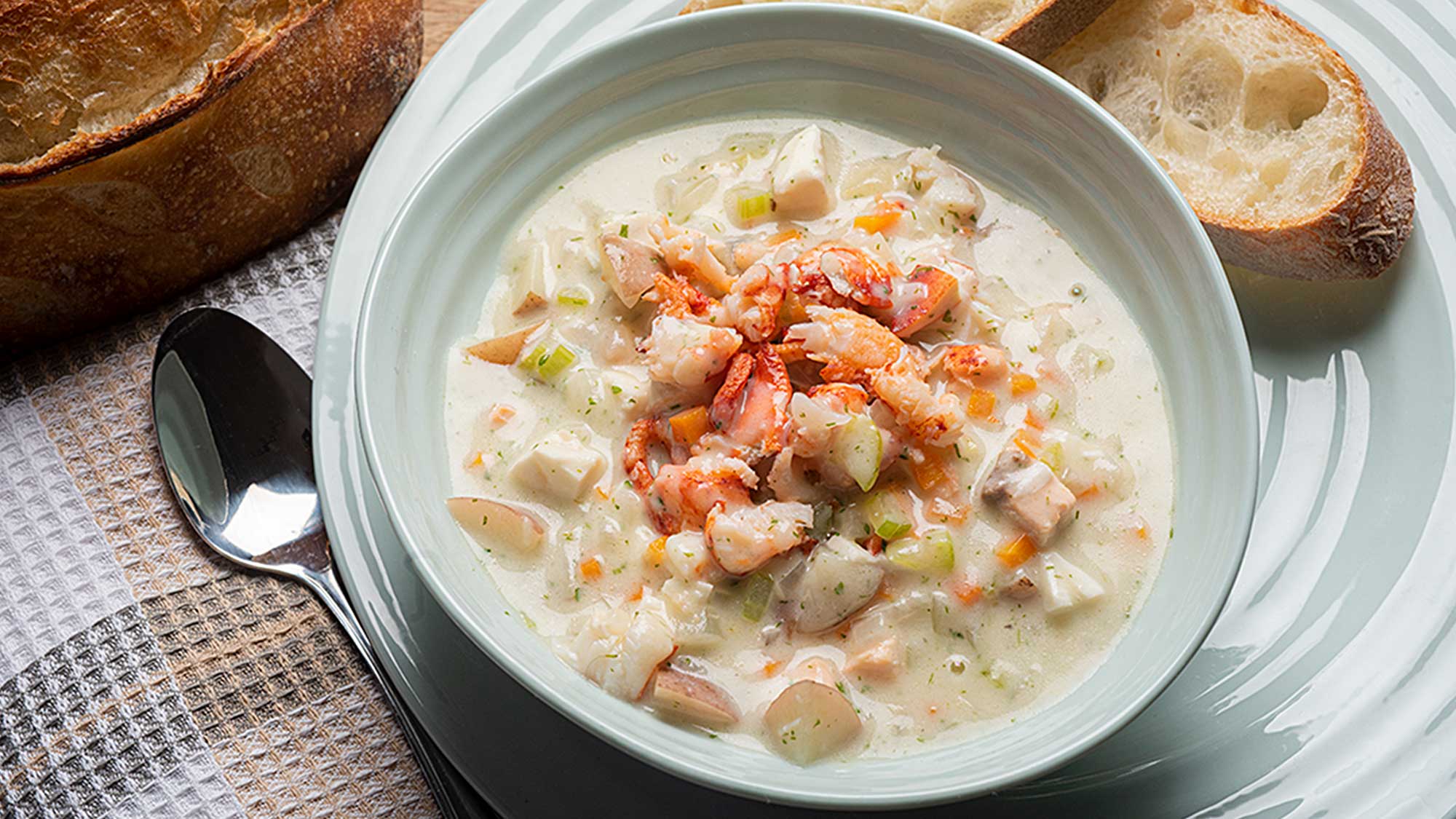 A bowl of seafood chowder with some baguette slices
